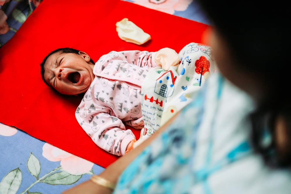 a baby yawns while laying on a red rug