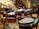 A set of electronic drums is positioned in an auditorium with tiered seating in the background. The room is spacious with wooden flooring and a series of black and white chairs organized in rows. The drum set, equipped with cymbals and multiple drum pads, is centrally placed on what appears to be a stage area.
