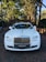 A luxurious white car is adorned with elegant wedding decorations, parked on a brick driveway under a canopy of tall trees. The background features a brick archway leading to a lush garden.