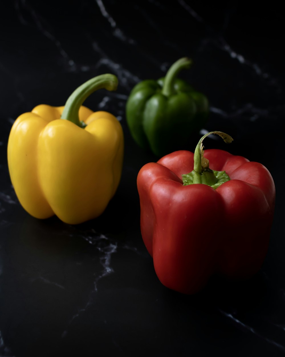 three different colored peppers on a black surface