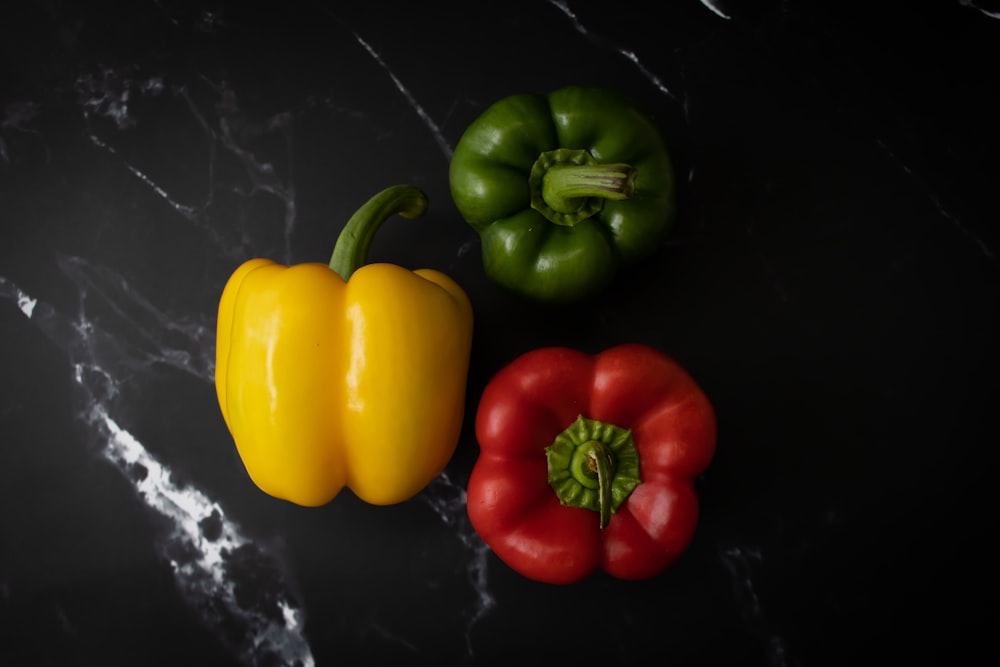 Tres pimientos de diferentes colores sobre una superficie negra