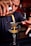 A bartender carefully pours a yellow cocktail mixture through a fine mesh strainer into a coupe glass. The focus is on the hands and the cocktail, capturing the precision and skill involved in the preparation. The bartender is in a dimly lit bar setting.