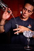 A focused student practicing pouring techniques during a bartending class in a professional setting.