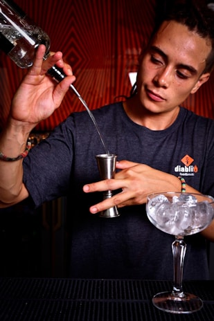 A focused student practicing pouring techniques during a bartending class in a professional setting.