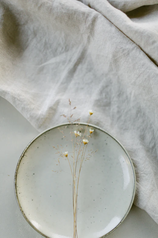 A glass dish and dried flowers on white linen