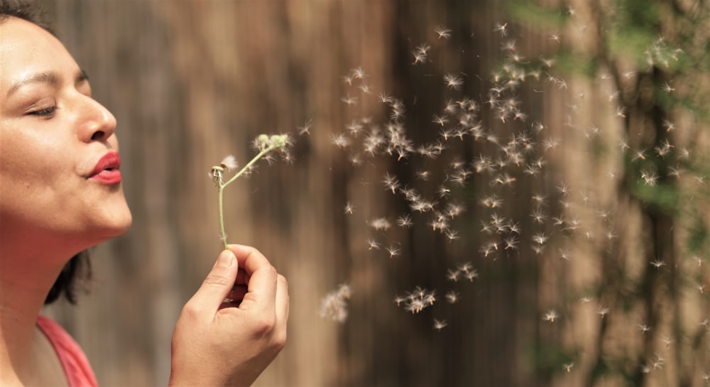 a woman blowing on a dandelion with her eyes closed