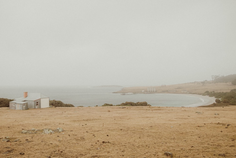 a lone house in a field with a body of water in the background