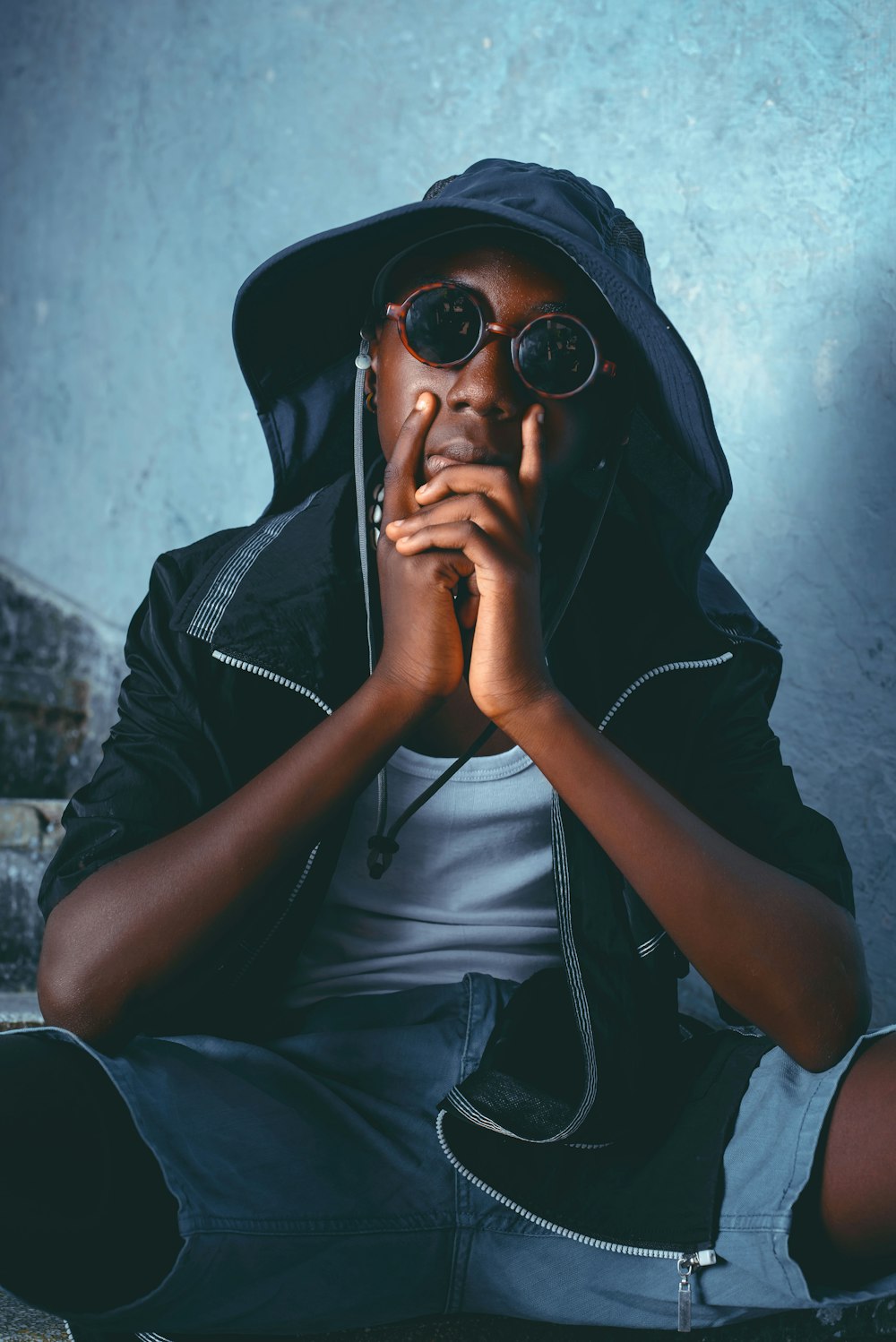 a man sitting on the ground wearing a hoodie and holding his hands to his