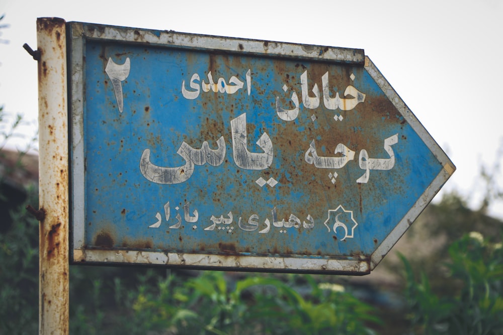 a rusted blue sign with arabic writing on it