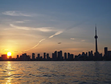 A sleek airplane soaring above the Toronto skyline at sunset.