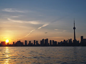 A warm sunset view of Toronto's skyline featuring the CN Tower with soft golden light reflecting on Lake Ontario.