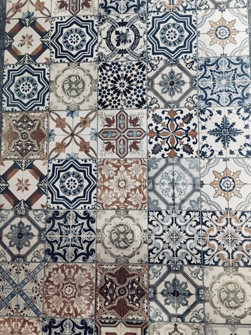 A collection of intricately designed ceramic tiles with various geometric and floral patterns. Each tile features unique motifs with combinations of blue, beige, and terracotta colors. The patterns range from symmetrical star shapes to more organic floral designs, providing a vintage and artistic appearance.