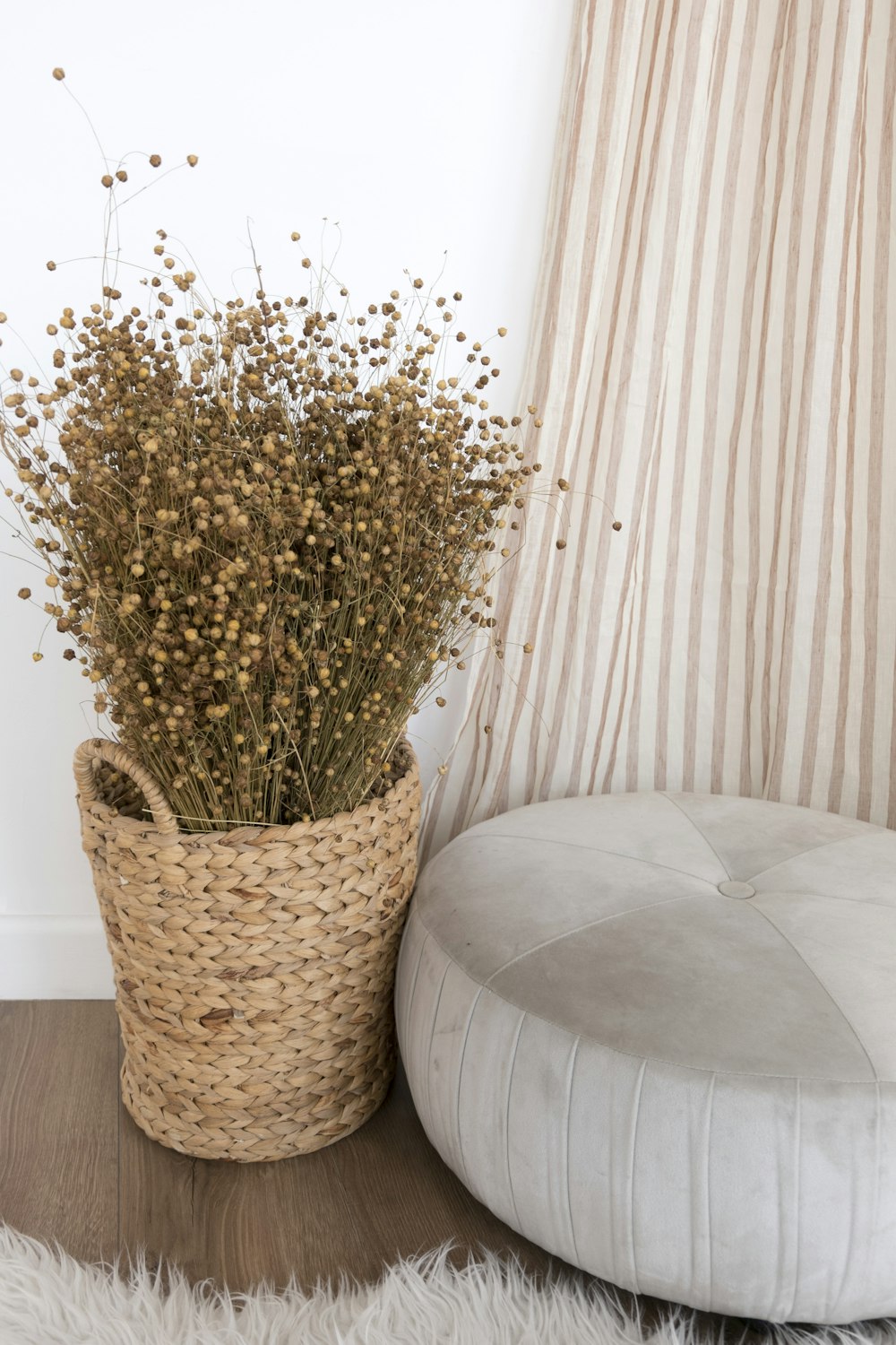 a plant in a basket next to a round ottoman