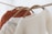 Three knit sweaters are hanging on wooden hangers. The sweaters are draped over a thick rope, showcasing their textures. The foreground sweater is cream-colored with a soft, fuzzy texture, while the middle sweater features cable knit details in a light beige hue. The rear sweater is a vibrant rust color.