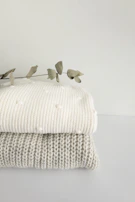 Delicate organic cotton baby clothes arranged on a wooden table with dried eucalyptus.
