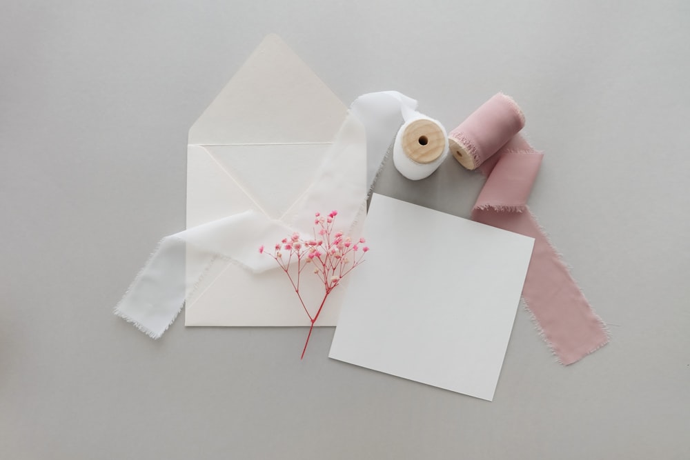 une enveloppe blanche avec une fleur rose et une paire de ciseaux à côté