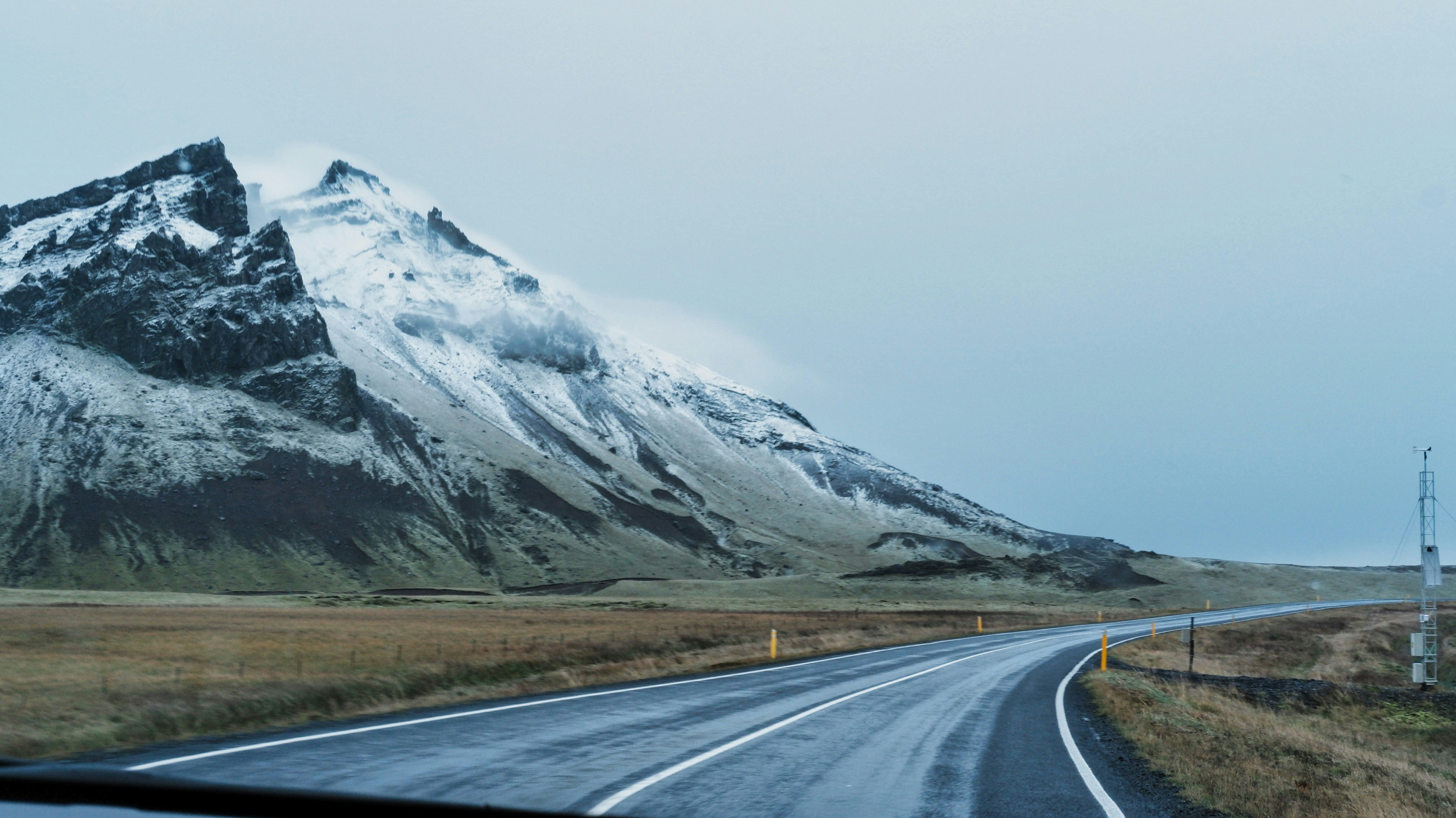 a car driving down a road next to a snow covered mountain