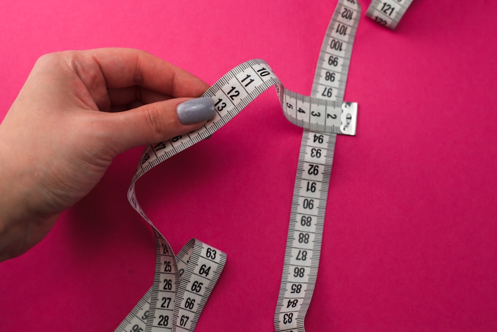 a person holding a measuring tape on a pink surface