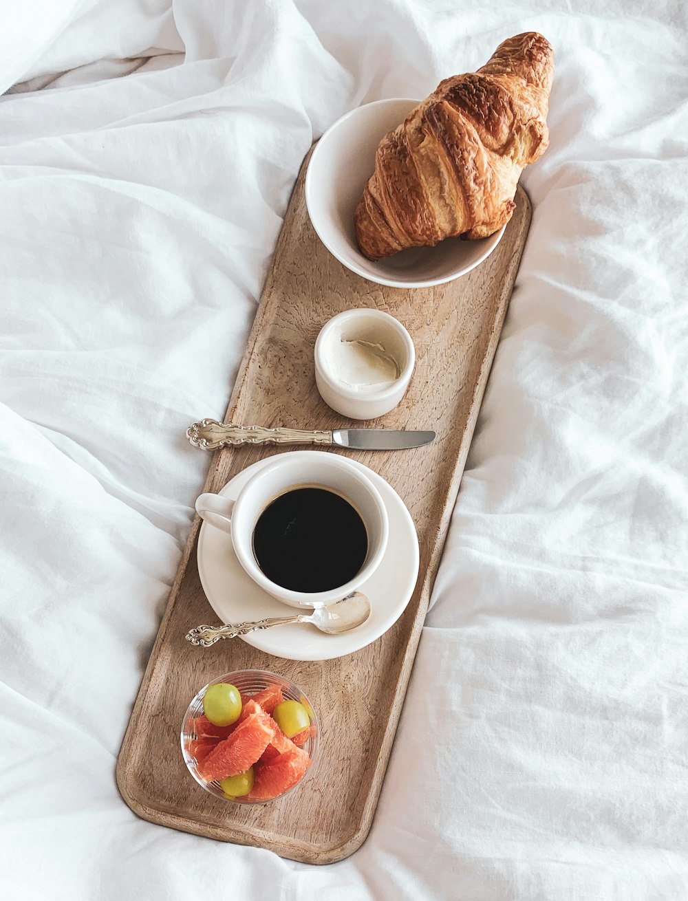 a tray with a croissant, coffee and fruit on it