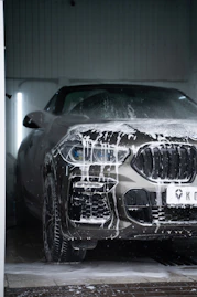 A grey car covered in white soap suds during a professional car wash