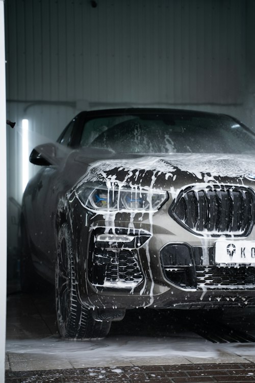 Close-up of a foam-covered gray BMW headlight and grille in a wash bay