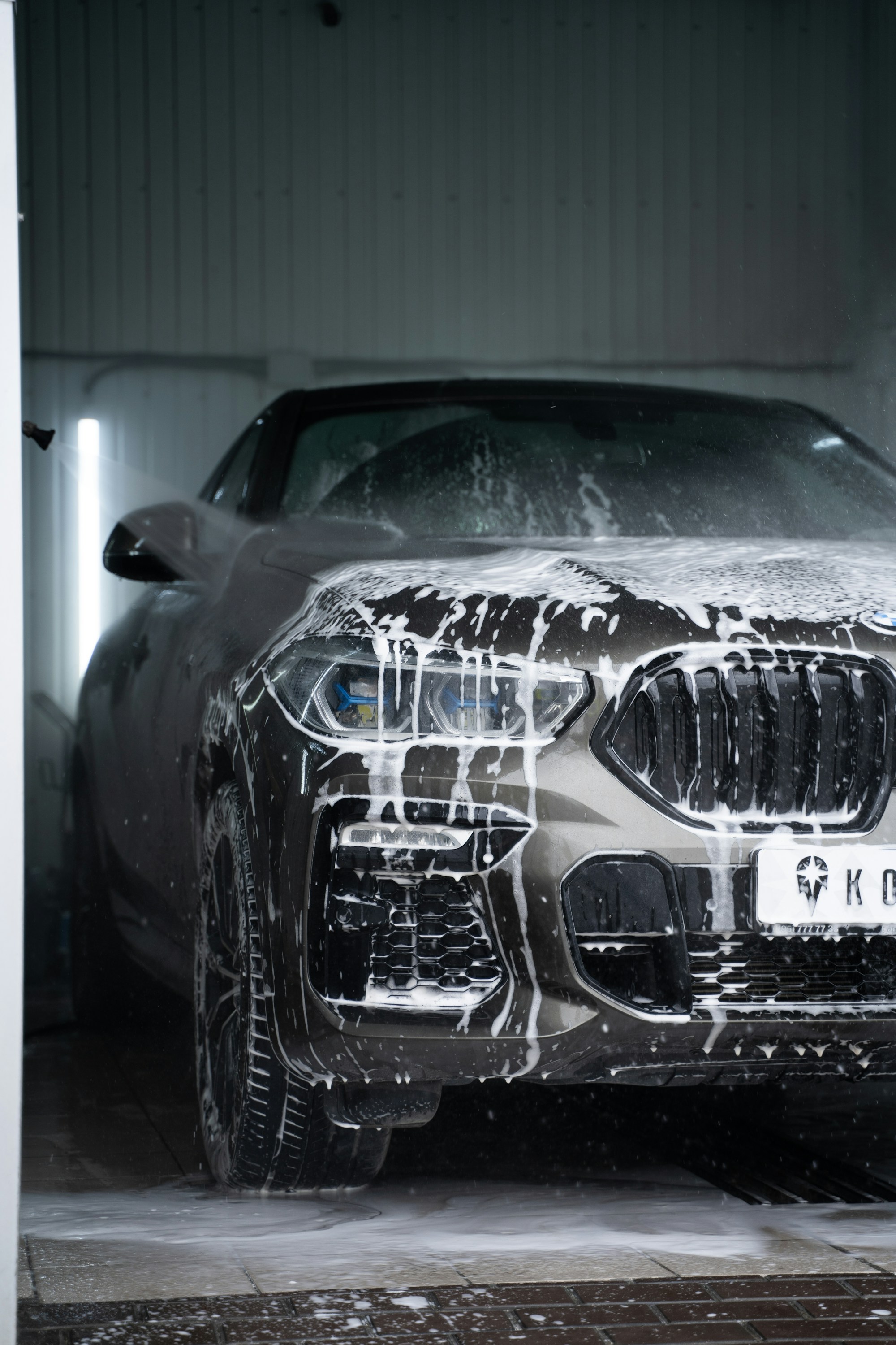 A grey car covered in thick white foam before its wash