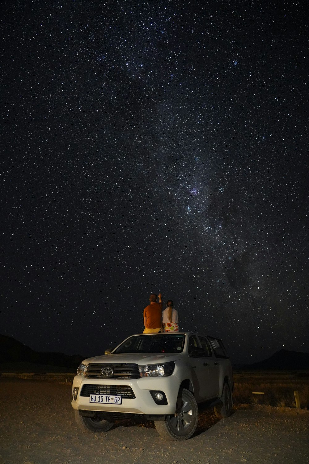 two people sitting on top of a vehicle under the stars