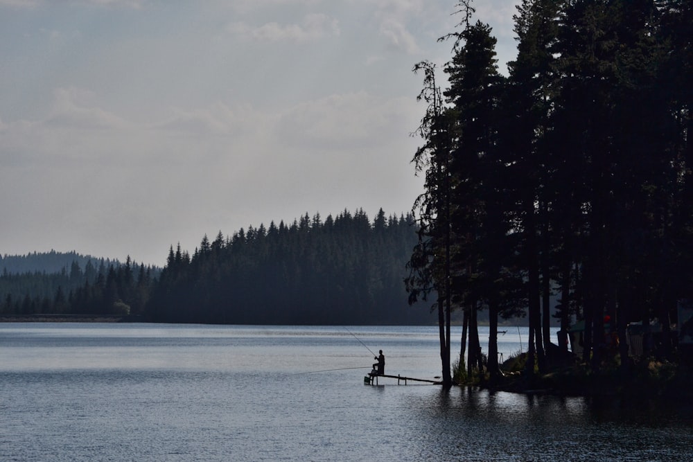 a man fishing on a lake surrounded by trees