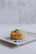 A neatly plated dish of risotto mixed with vegetables such as carrots and green beans, garnished with a fresh basil leaf, on a decorative white and blue ceramic plate with a marble background.