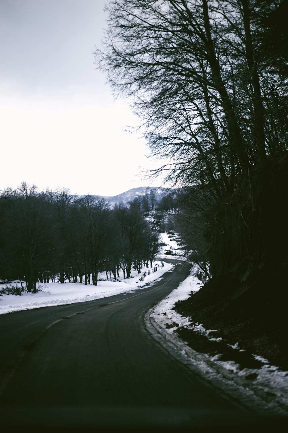 a snowy road with trees and a hill in the background