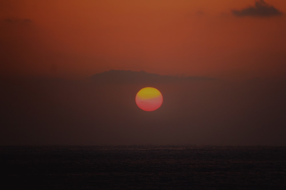 the sun is setting over the ocean on a cloudy day