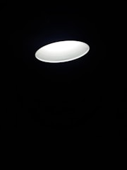 A single bright circular ceiling light fixture illuminates against a dark background, creating a contrast between the light and shadow.
