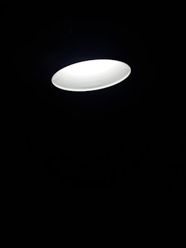 A single bright circular ceiling light fixture illuminates against a dark background, creating a contrast between the light and shadow.
