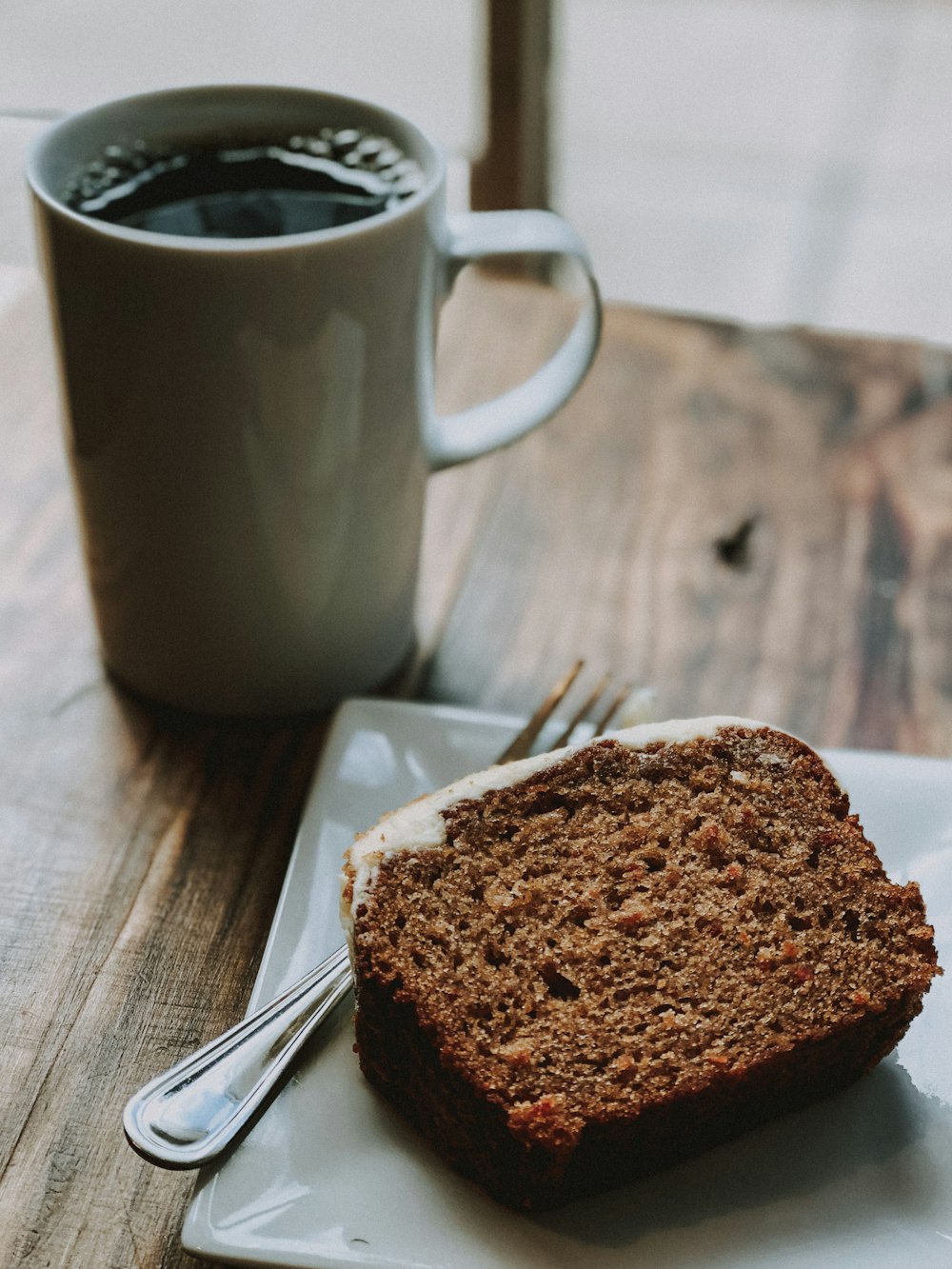 a piece of bread on a plate next to a cup of coffee