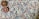 A close-up view of a knitted fabric featuring a textured pattern with a mix of colors including purple, blue, and beige. Two decorative circular buttons with intricate, colorful patterns are attached, providing a contrast against the muted tones of the fabric.