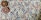 A close-up view of a knitted fabric featuring a textured pattern with a mix of colors including purple, blue, and beige. Two decorative circular buttons with intricate, colorful patterns are attached, providing a contrast against the muted tones of the fabric.