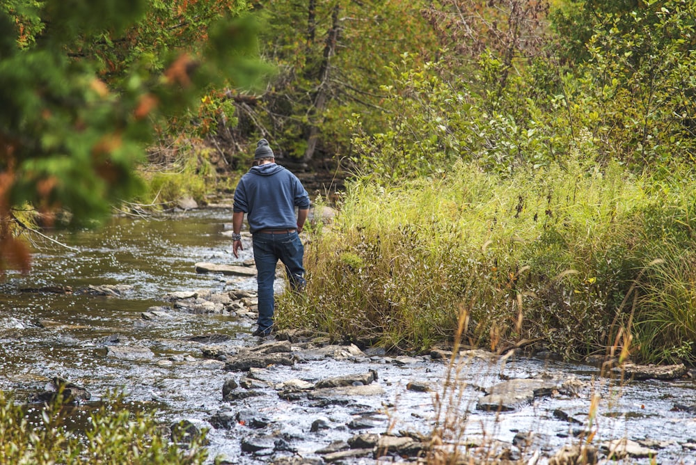 a man walking across a river next to a forest