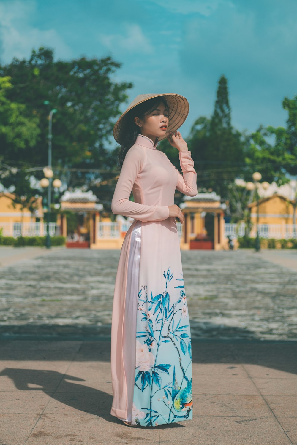 a woman in a dress and hat standing on a sidewalk