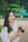 A happy woman holding a camera outdoors, smiling after a personalized photo workshop.