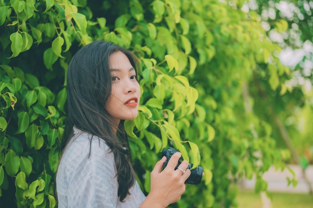 a woman standing in front of a bush holding a camera