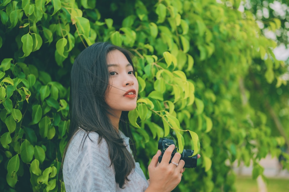 a woman standing in front of a tree holding a camera