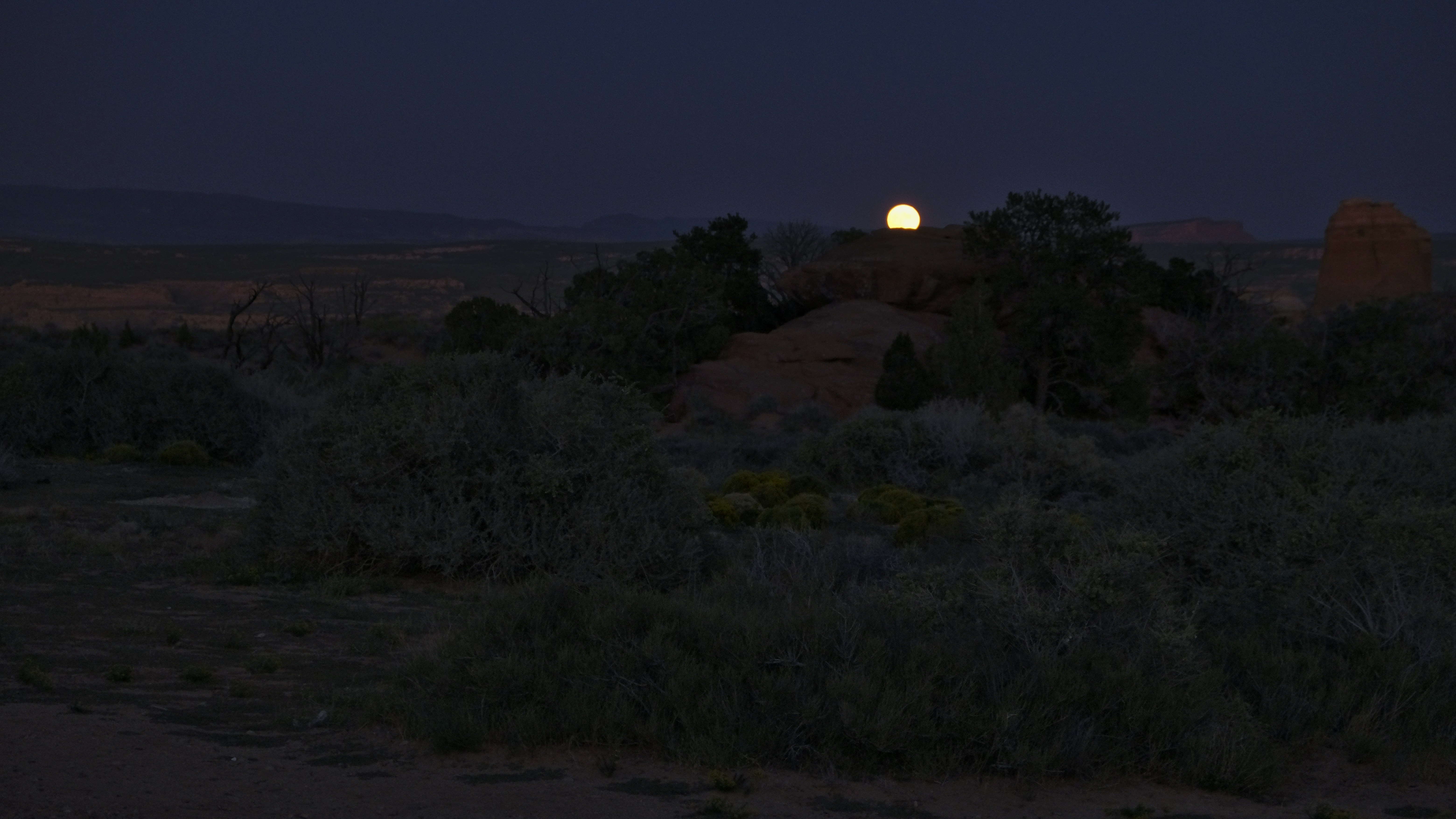 a full moon rises over a desert landscape