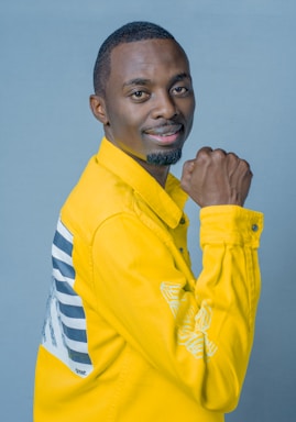 A person is wearing a bright yellow jacket with a graphic design on the back. They are smiling and appear to be posing confidently against a light blue background.