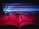 An open book is positioned with a pair of black-rimmed glasses resting on its pages. Colorful, neon light streaks of blue, purple, and pink pass through the air above, creating a dynamic play of light and shadow on the pages.