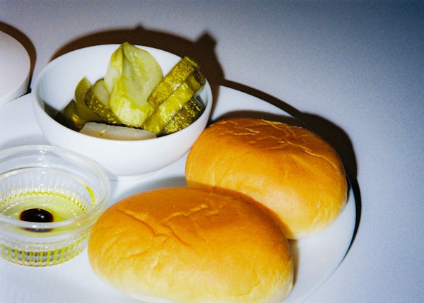 A white plate topped with two rolls and a bowl of pickles