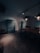 A dimly lit room with industrial-style lighting and minimal furnishings. There are two large, teal-colored cabinets against the wall. A wooden table with metal chairs is set in the center of the room, creating a functional yet sparse appearance.