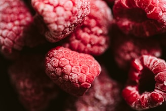 A close-up of frozen raspberries glistening with frost on a rustic wooden table.
