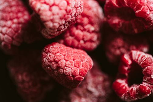A close-up of frozen raspberries glistening with frost on a rustic wooden table.