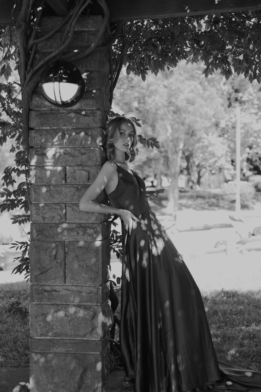 a woman in a long dress leaning against a brick wall