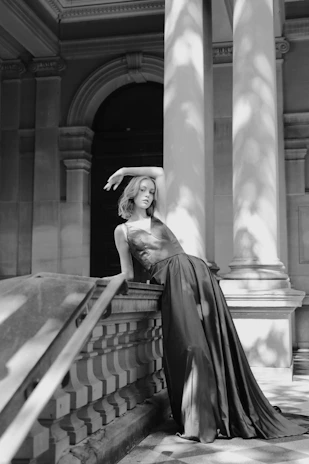 Artistic black-and-white editorial shot featuring a poised model in a flowing gown against a marble backdrop.